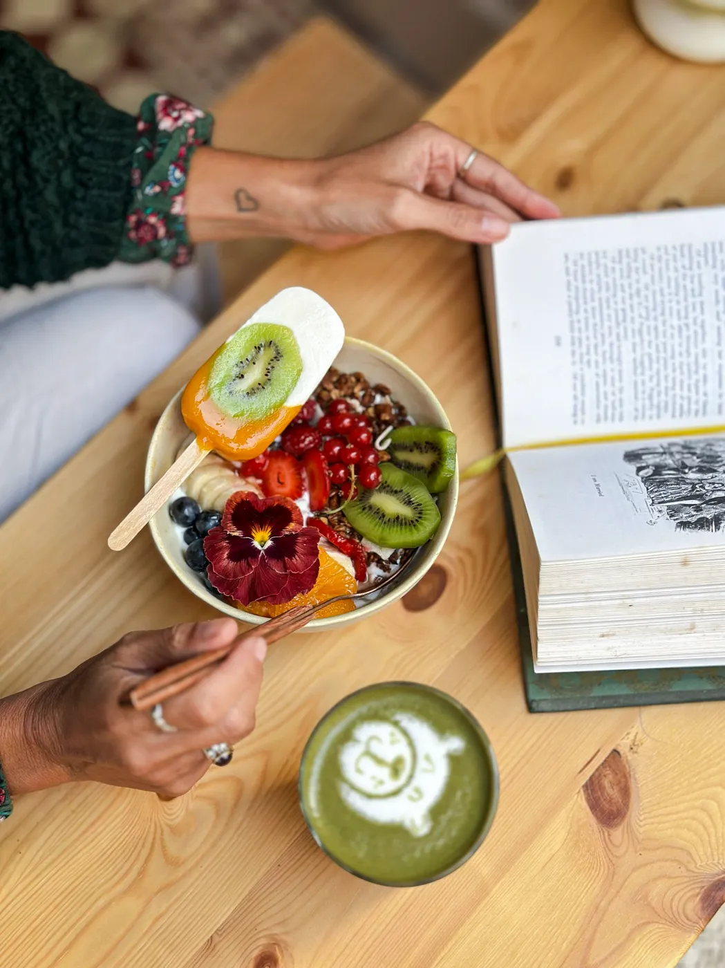 Bowl de fruta ao lado de um livro aberto e um matcha latte