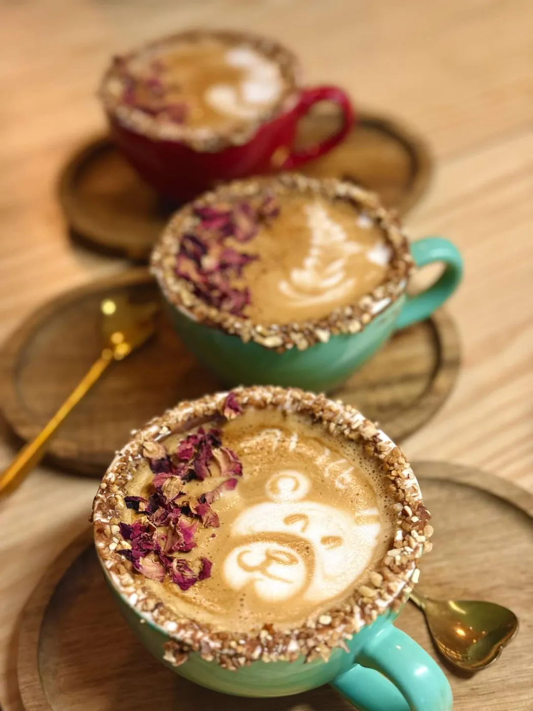 Três cafés com latte art e pétalas de rosa