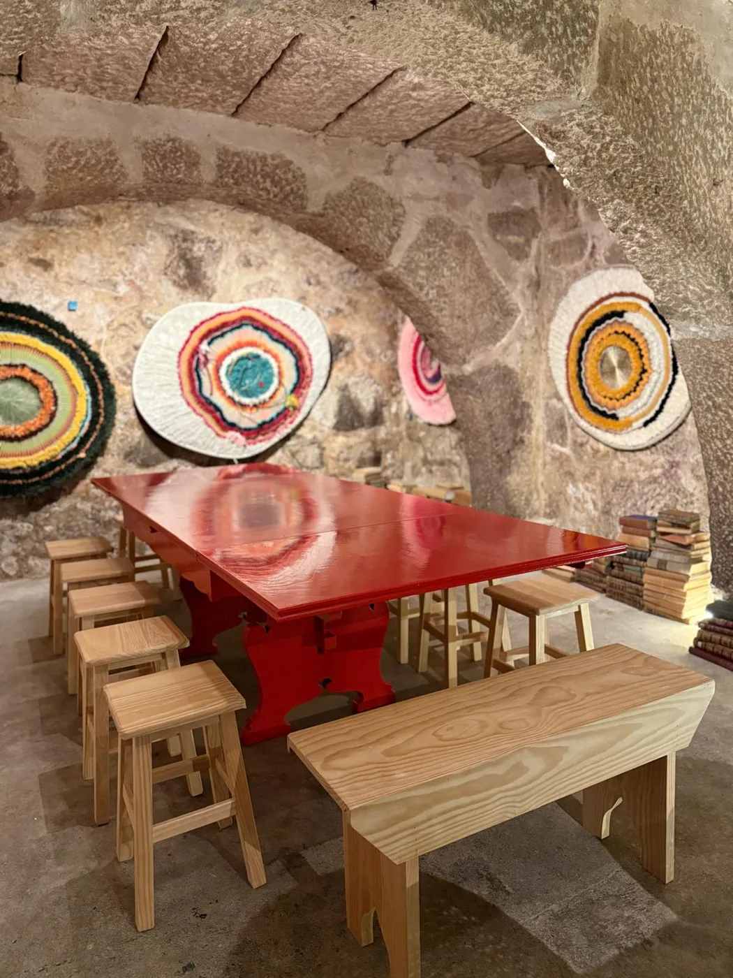 A sala privada: mesa vermelha sob uma abóbada de pedra, com discos tecidos na parede