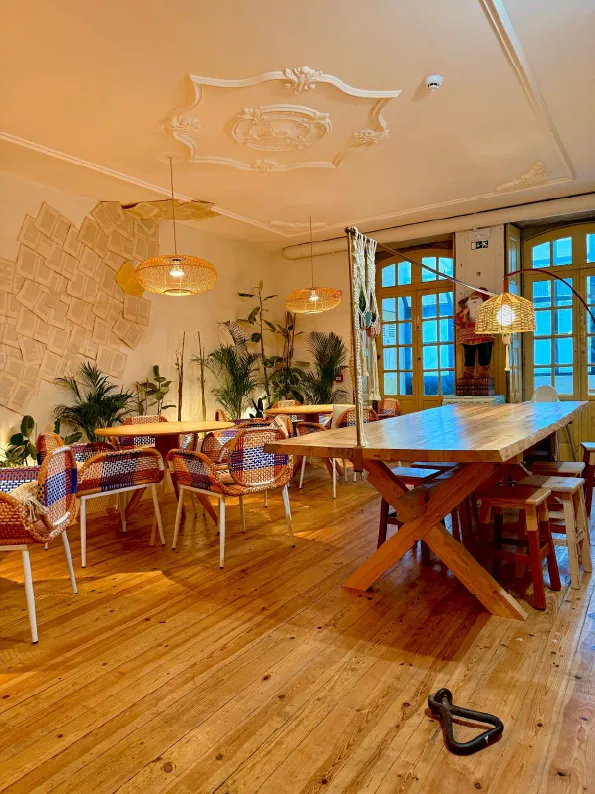 A sala principal: mesas de madeira, candeeiros de rattan e plantas junto às portadas